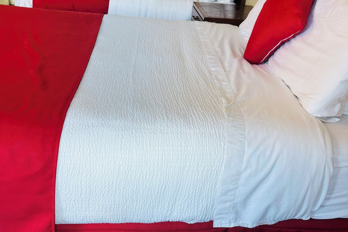 Ein Hotelzimmer mit zwei Betten, jeweils mit roter und weißer Bettwäsche, und einem Nachttisch dazwischen.