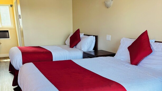 A hotel room with two beds, each with red and white bedding, wooden headboards, and a small bedside table. - Imperial Motel (100 Mile House)