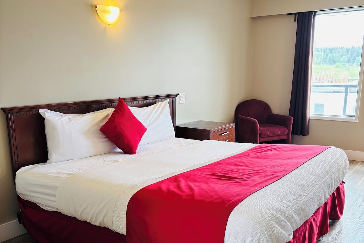 Ein Hotelzimmer mit einem großen Bett, einem Nachttisch, einem Sessel und einem Fenster mit Blick.