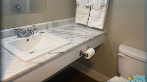 A bathroom with a marble sink, a toilet, and two towels hanging on a towel rack. - Imperial Motel (100 Mile House)