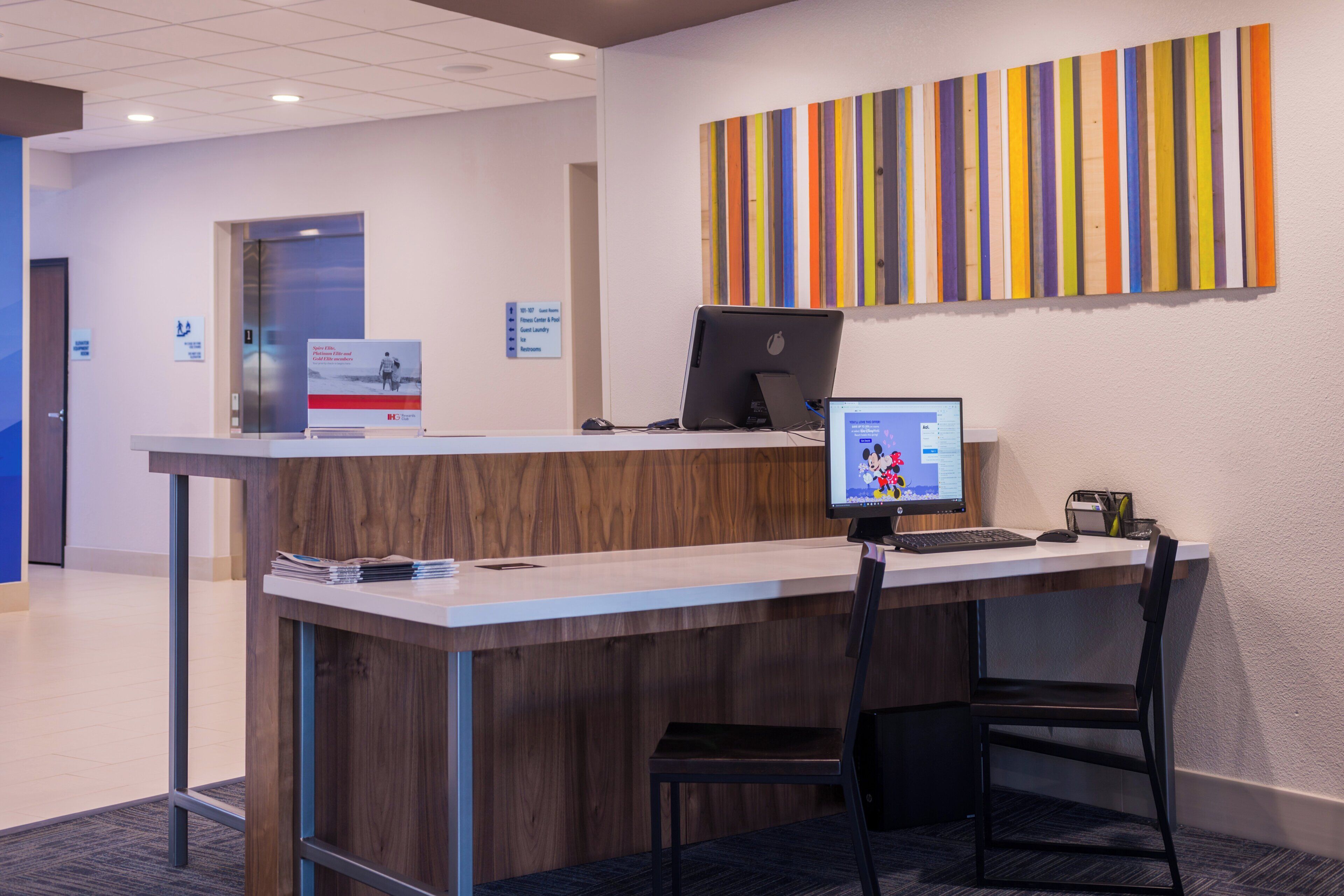 Un mostrador de recepción con una computadora, una silla y un letrero que indica los servicios para huéspedes.
