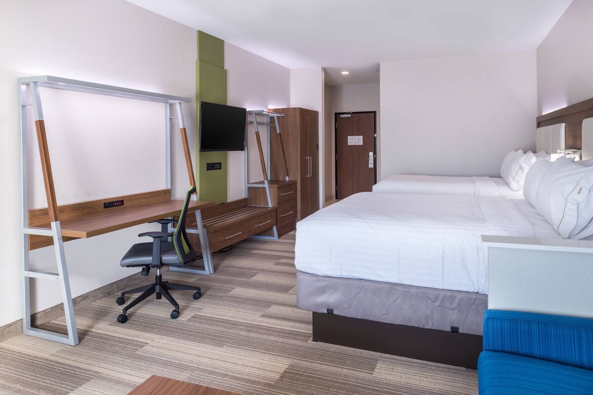 A hotel room with a bed, a desk with a chair, a TV mounted on the wall, and a wardrobe.