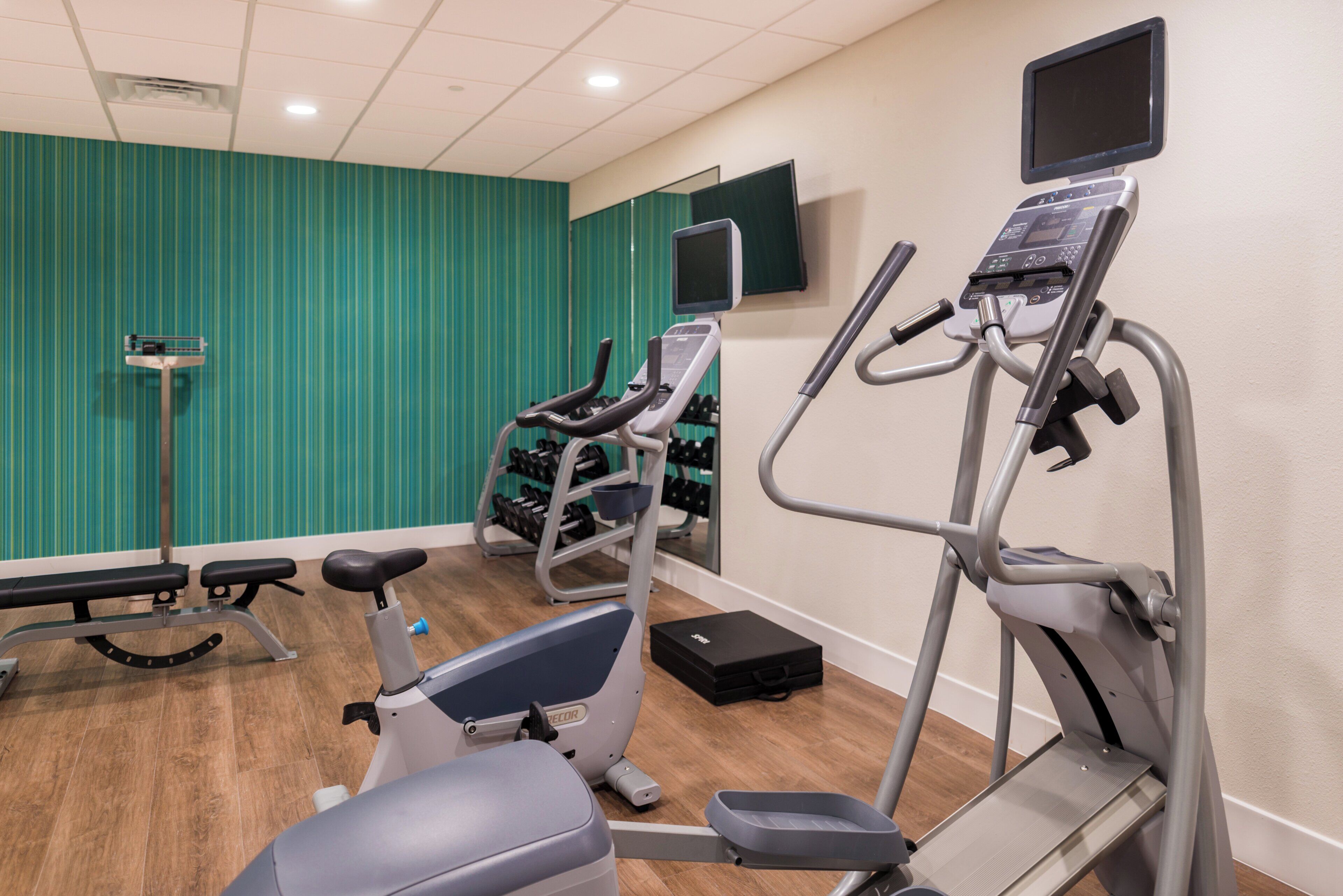 A gym with cardio equipment, a bench, and a wall-mounted TV.
