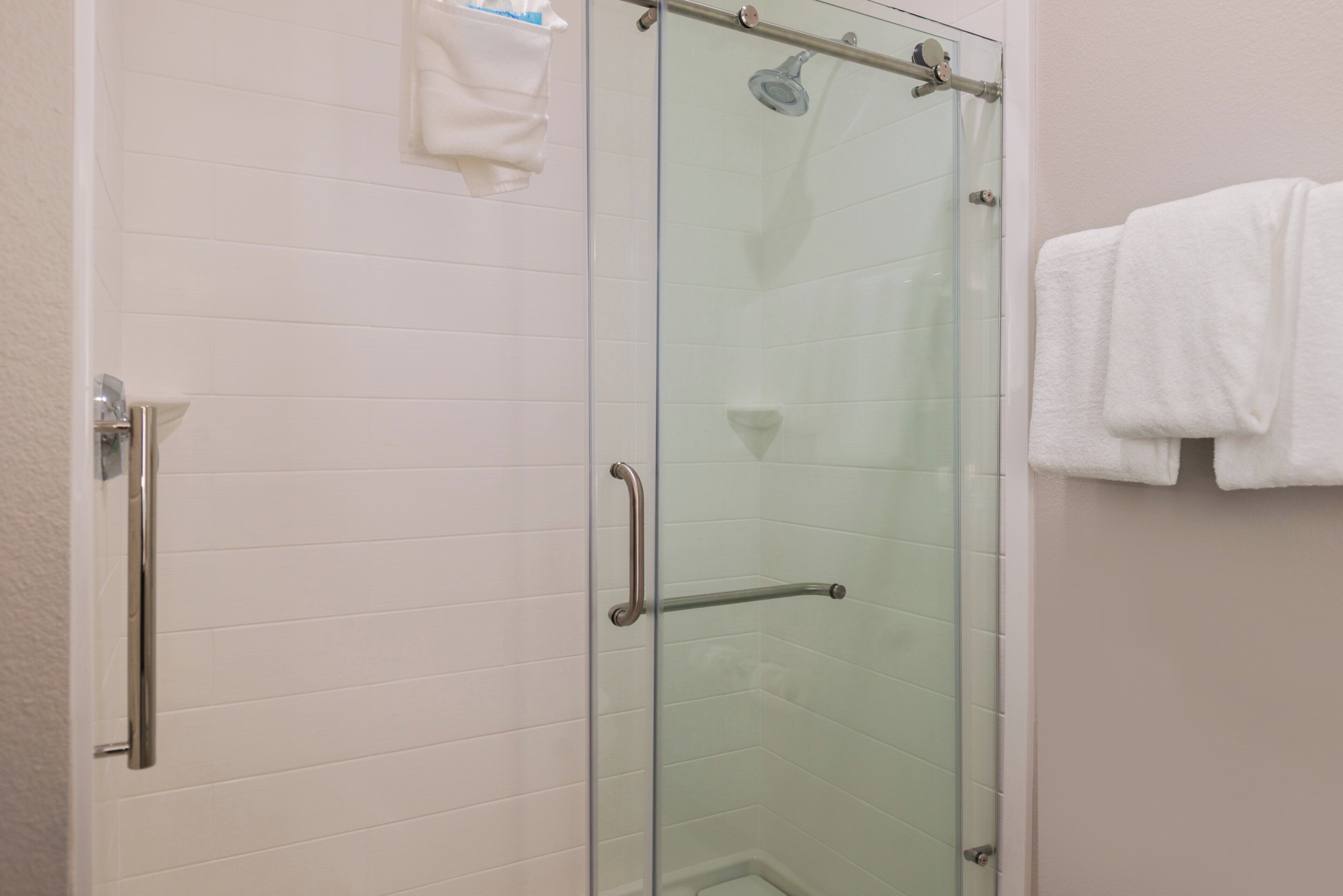 A glass-enclosed shower stall with a handheld showerhead, a towel rack, and a towel hanging on the wall.