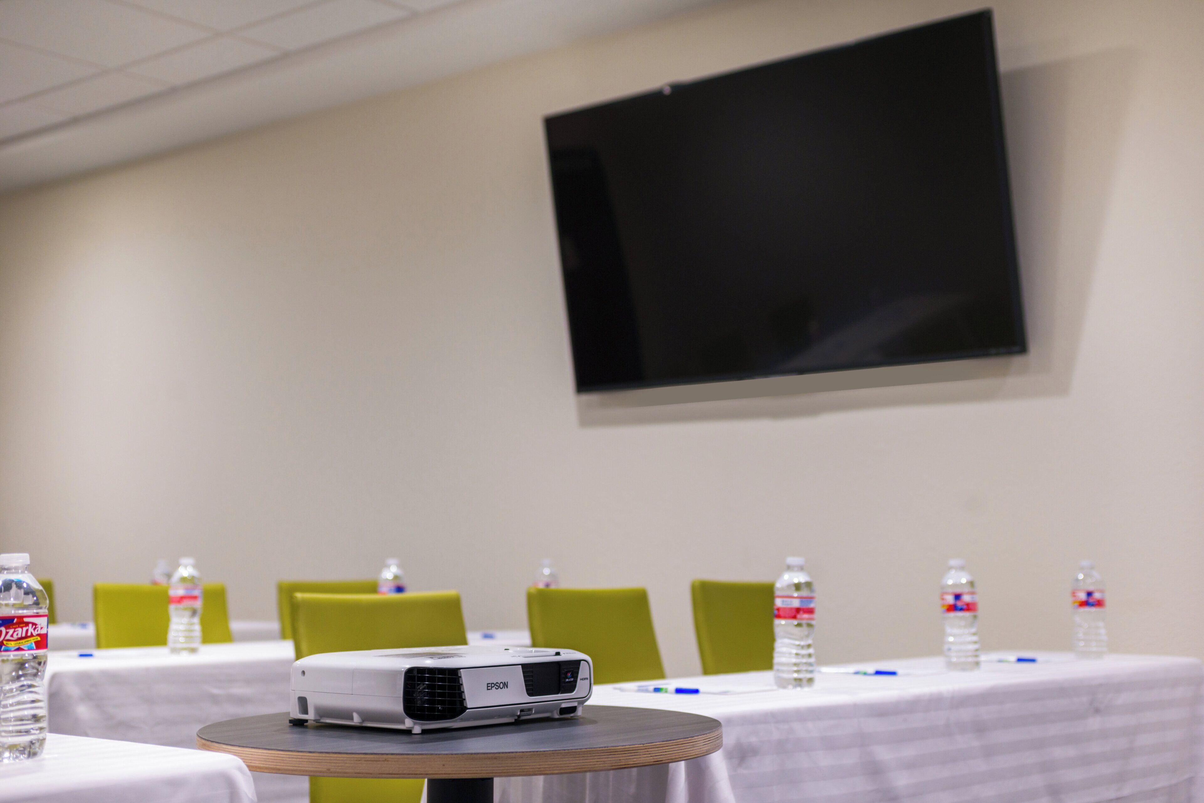 A conference room with a projector on a table, water bottles, and green chairs.