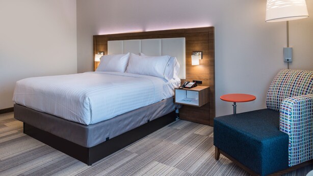 A hotel room with a large bed, a bedside table with a lamp, a small round table, and a colorful chair. - Holiday Inn Express & Suites Fort Worth West by IHG (Fort Worth)