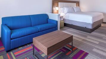 A hotel room with a blue sofa, a wooden side table, a bed with white bedding, and a colorful striped carpet.