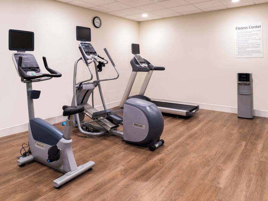 Centro de fitness com esteiras, elípticos e bebedouro.