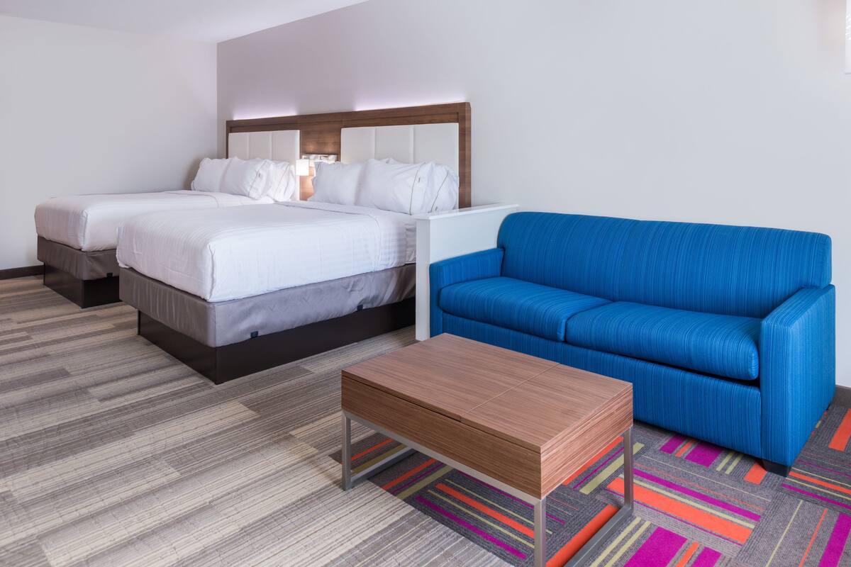 A hotel room with two beds, a blue sofa, and a wooden coffee table.