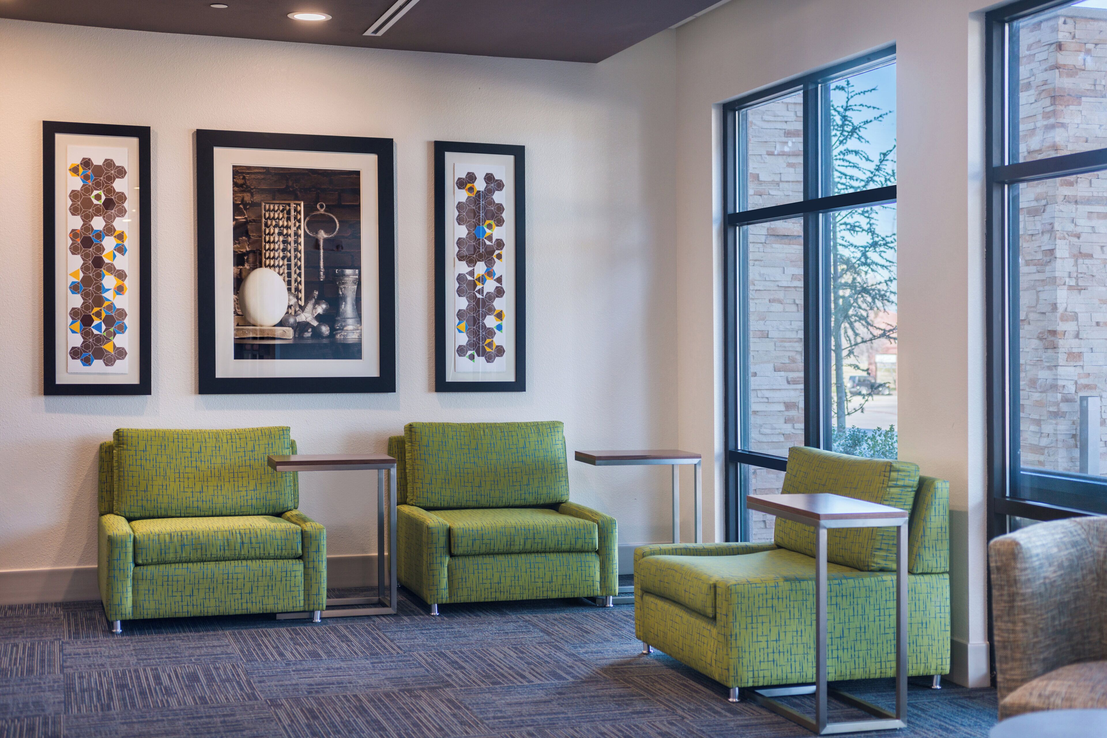A modern waiting area with green upholstered chairs, a small table, and framed artwork on the wall.