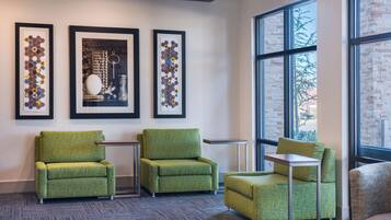 A modern waiting area with green upholstered chairs, a small table, and framed artwork on the wall.