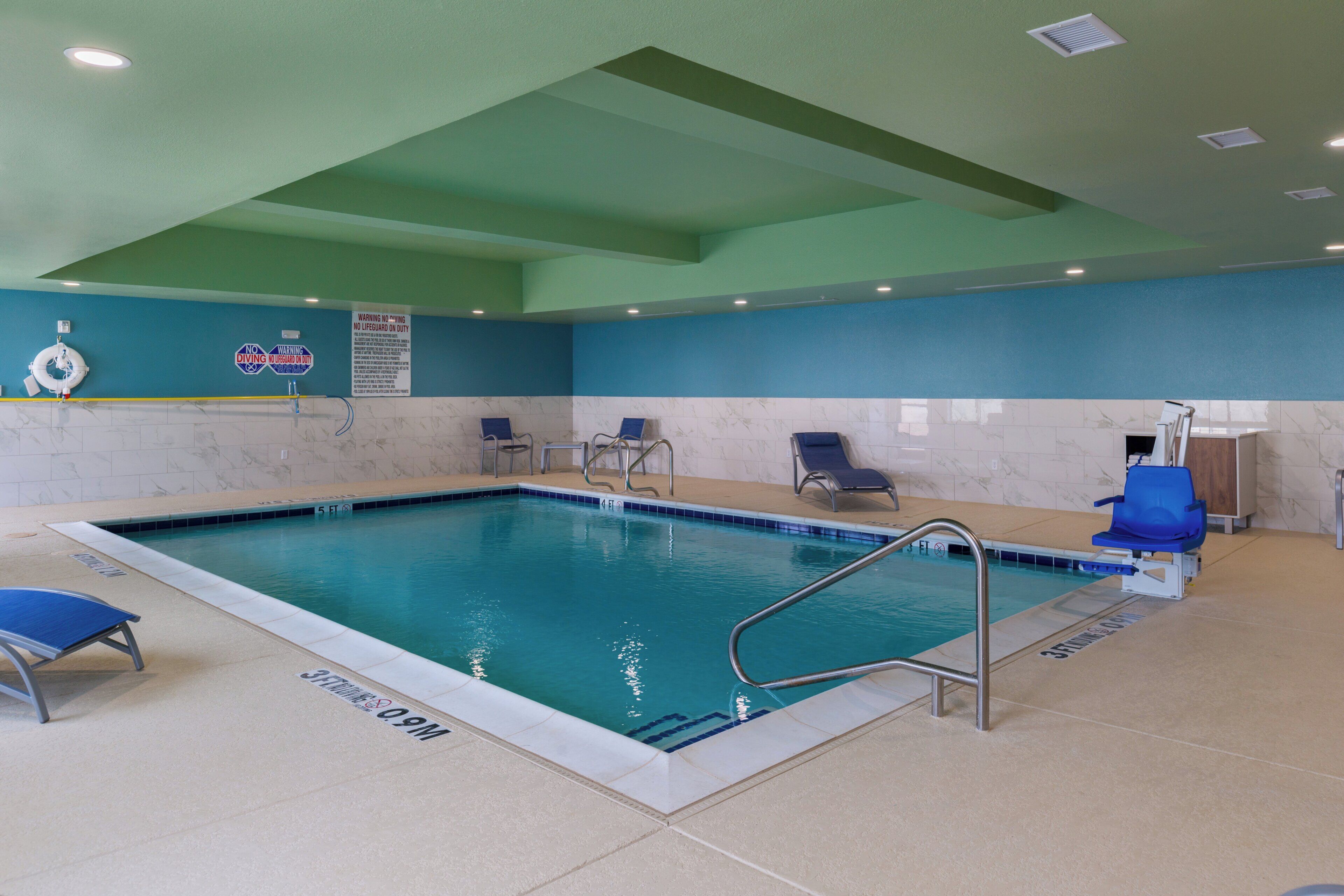 An indoor swimming pool with clear water, a diving board, and a lifeguard stand.