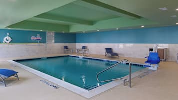 An indoor swimming pool with clear water, a diving board, and a lifeguard stand.