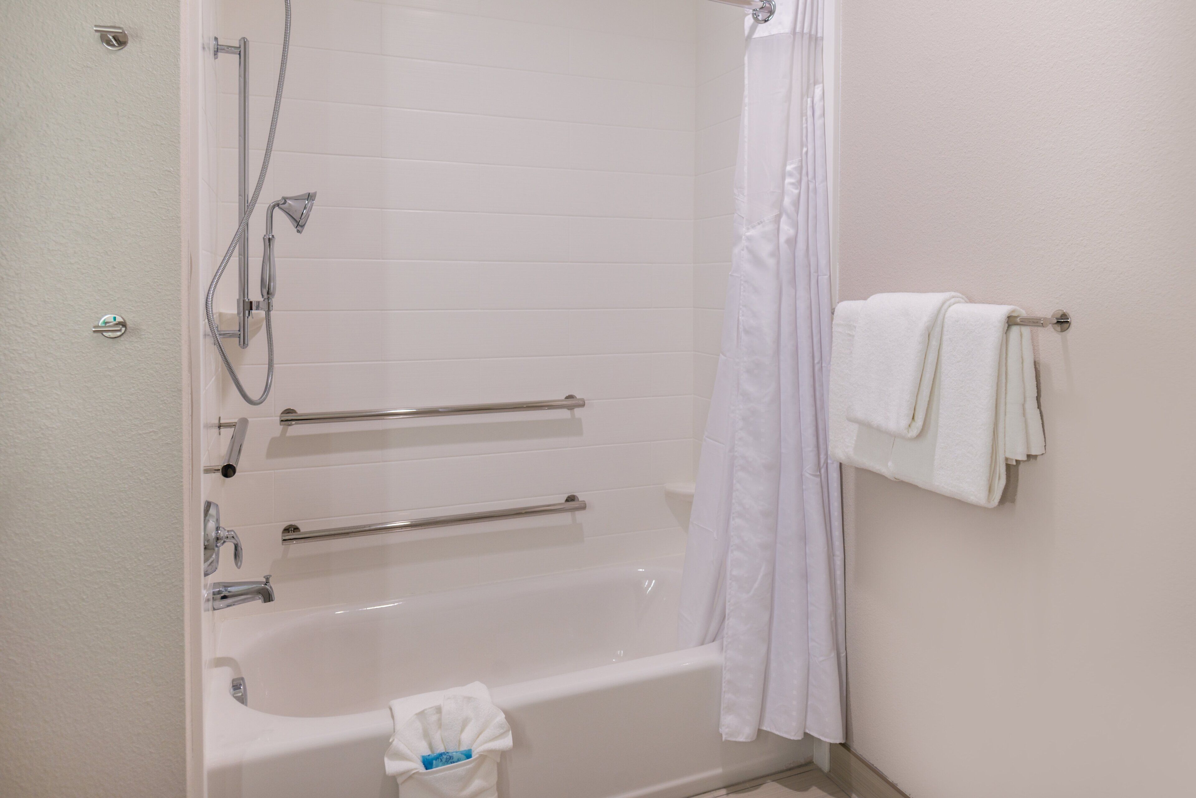 A standard bathroom with a bathtub, shower, grab bars, and a towel rack.