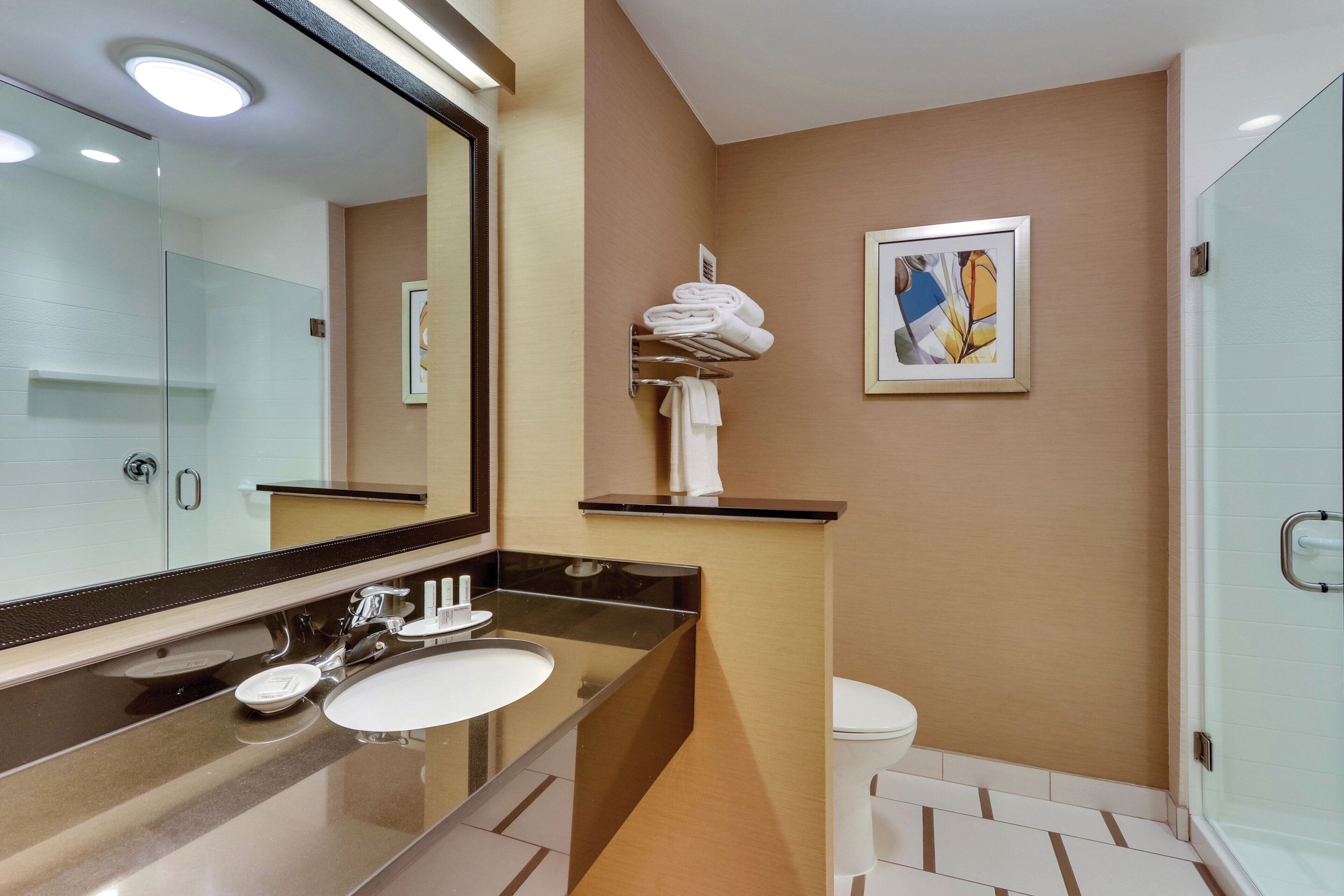 Un baño moderno con un espejo grande, un lavabo, un inodoro y una cabina de ducha con mampara de vidrio.