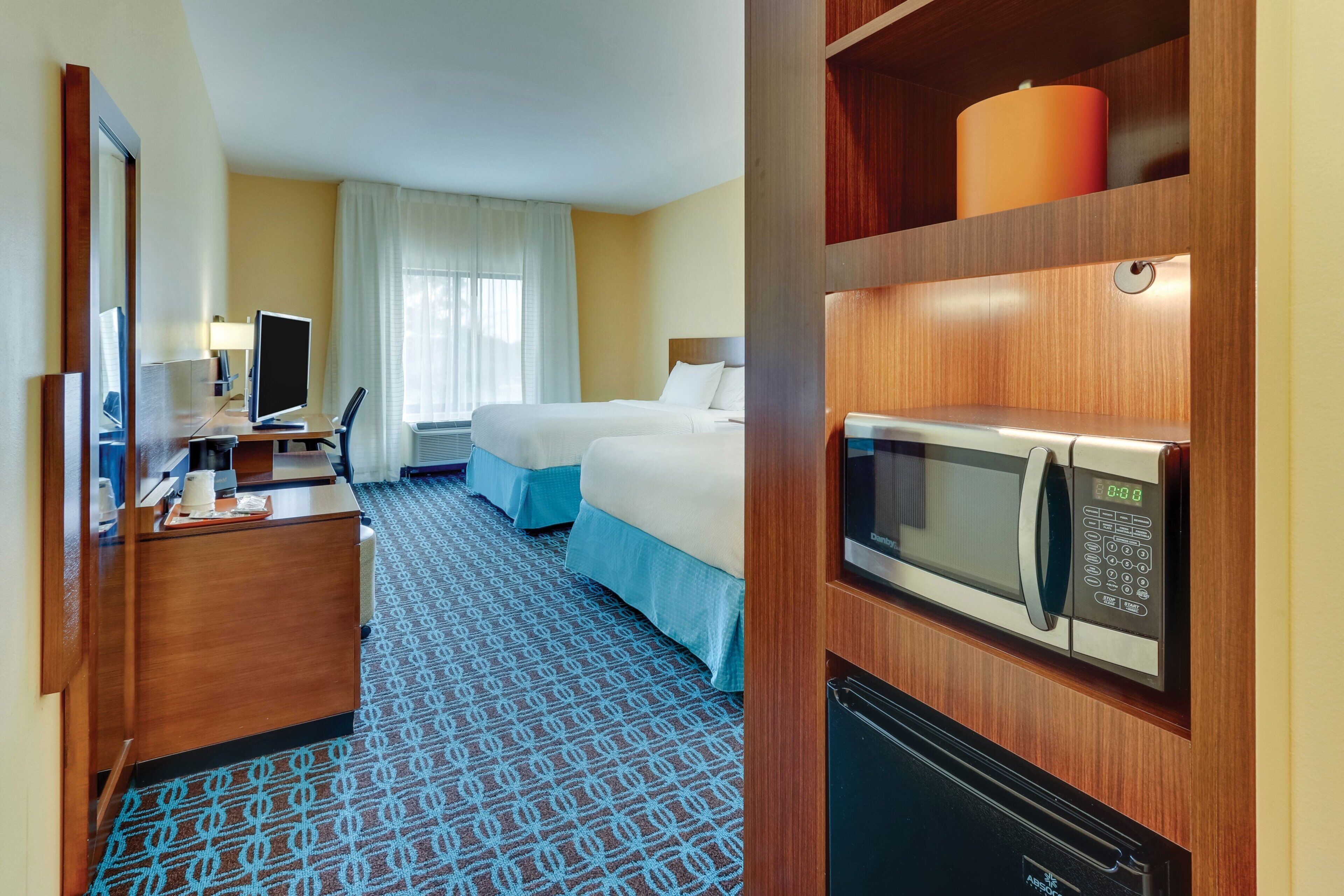 A hotel room with a desk, two beds, a microwave, and a refrigerator.