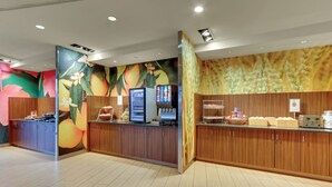 A modern breakfast area with wooden cabinets, a digital menu display, and a fruit-themed wall. - Fairfield Inn & Suites Dunn I-95 (Dunn)