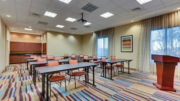 Un salón de conferencias con varias mesas y sillas, un atril y un amplio ventanal con cortinas.