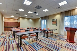 Un salón de conferencias con varias mesas y sillas, un atril y un amplio ventanal con cortinas.