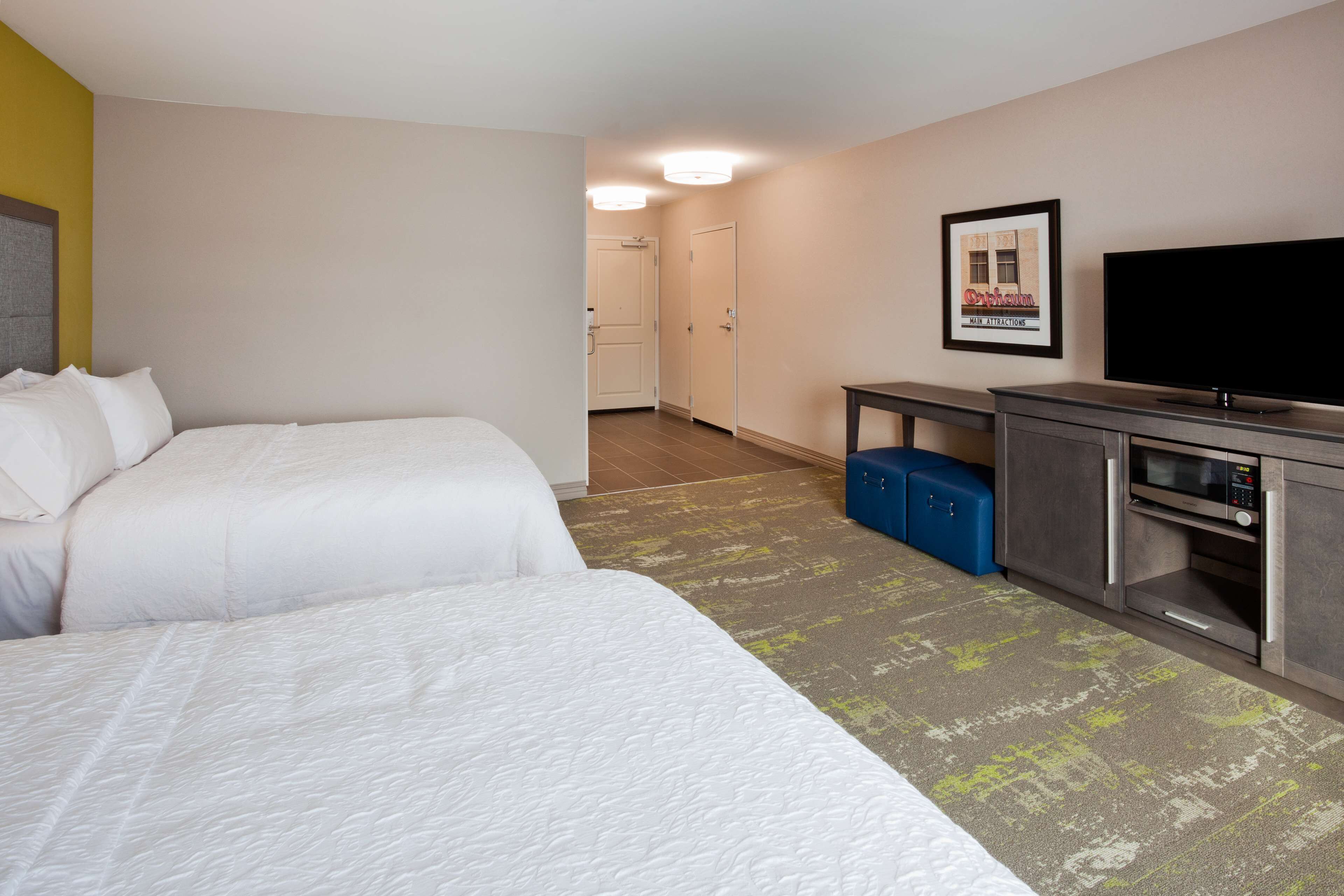 A hotel room with two beds, a television, a microwave, and a framed picture on the wall.