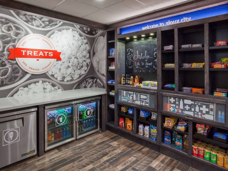 A snack bar with a chalkboard menu, ice cream display, and shelves stocked with various snacks and drinks.