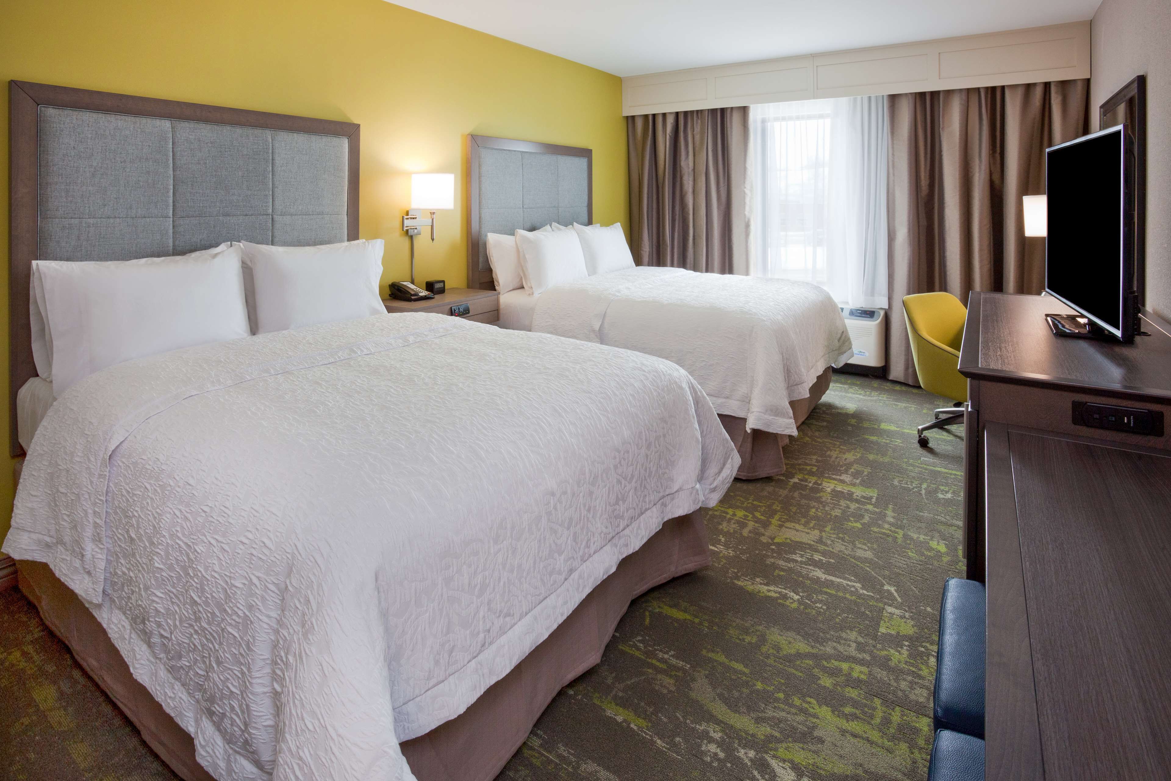 A hotel room with two beds, a desk, a chair, and a TV.