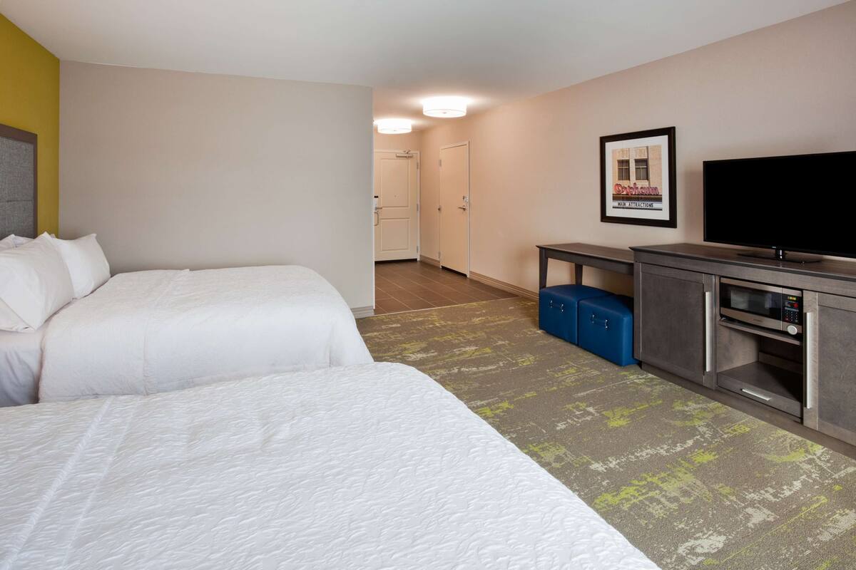 A hotel room with two beds, a television, a microwave, and a small desk.