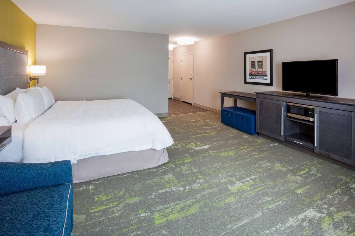 A hotel room with a bed, a desk, a television, and a framed picture on the wall.