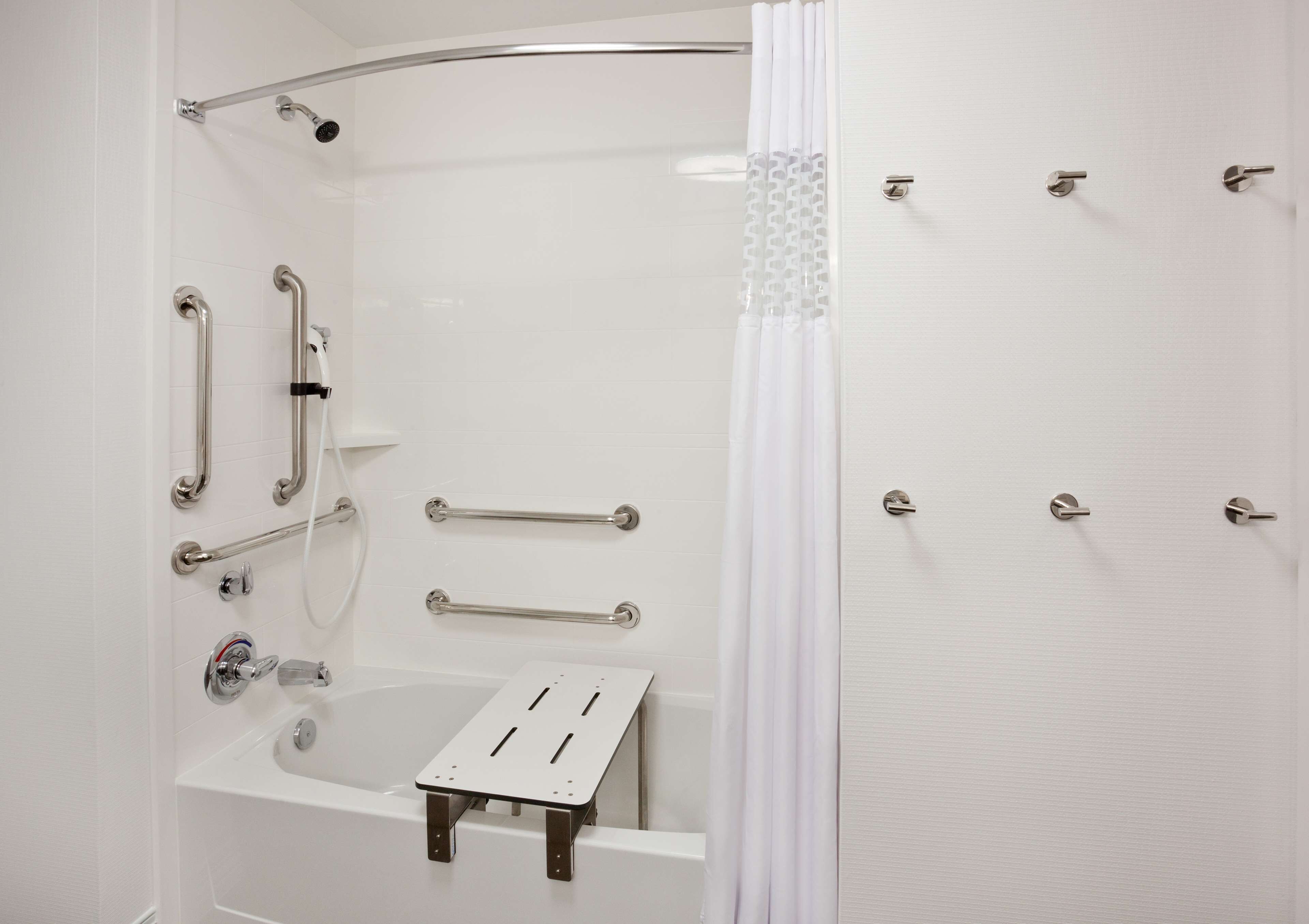 A modern bathroom with a walk-in shower, grab bars, a bathtub with a shower seat, and a white shower curtain.