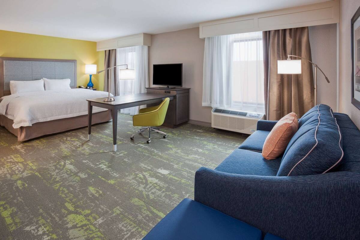A hotel room with a bed, a desk, a chair, a sofa, and a TV.