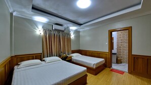 Habitación de hotel con dos camas individuales, ventilador de techo, aire acondicionado, piso de madera y felpudo.