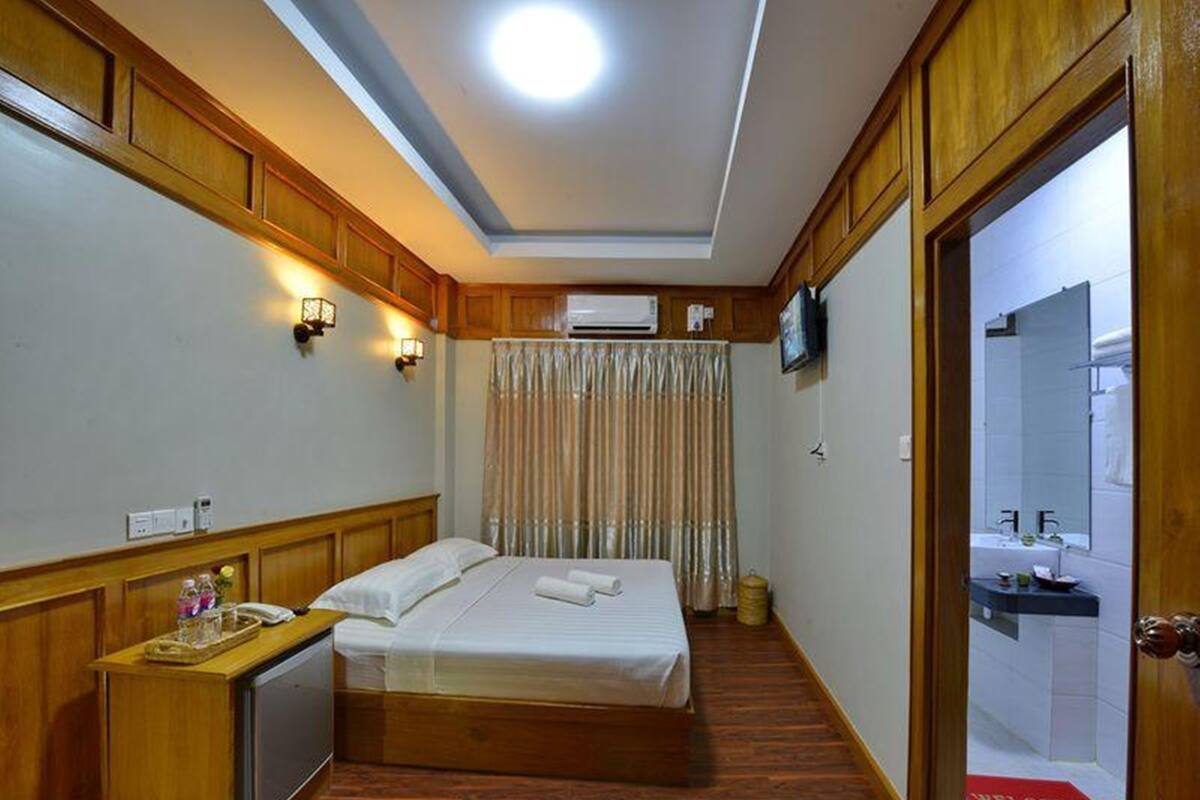 A hotel room with a wooden bed, bedside table, and a TV mounted on the wall.