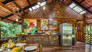 Une cuisine rustique aux murs en bois, avec un réfrigérateur et une table à manger dressée avec des fruits et des légumes.