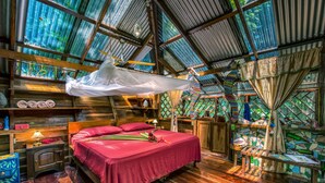 A rustic wooden room with a bed, a hanging chair, and a small table. - Congo Bongo EcoVillage Costa Rica (Cahuita)