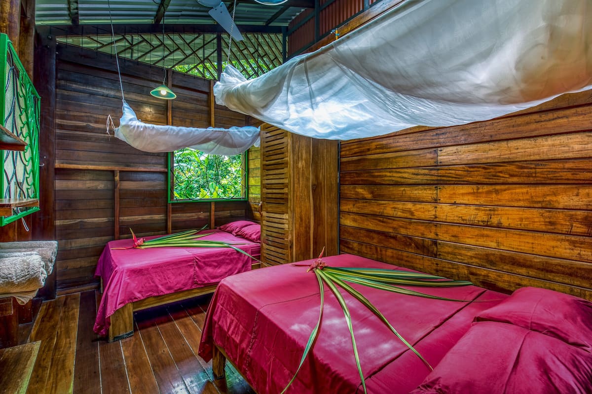 A room with two beds, each covered with a red bedspread and a white canopy.
