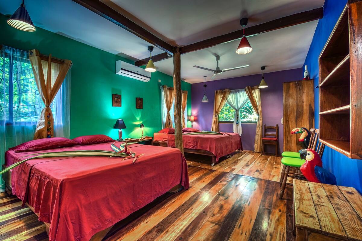 A room with two beds, wooden flooring, ceiling fans, and a bird-shaped chair.