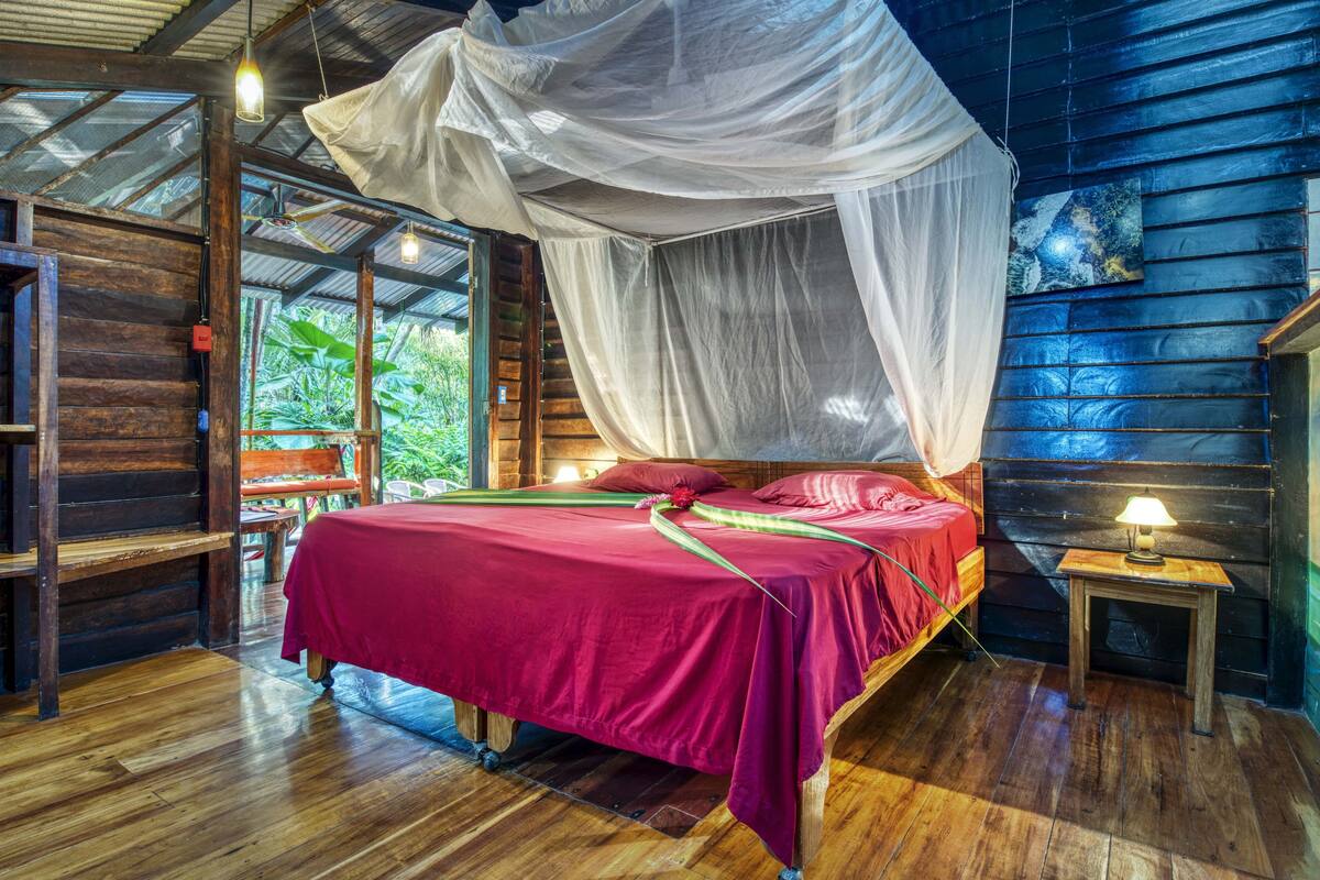 A wooden cabin bedroom with a bed, bench, and a small table with a lamp.