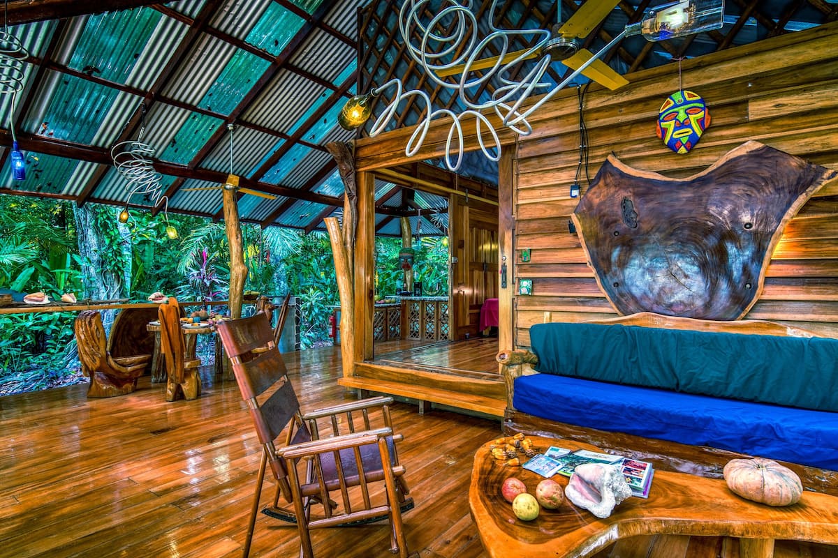 A wooden interior with a large wooden sculpture, a blue sofa, and a wooden table with fruits and magazines.