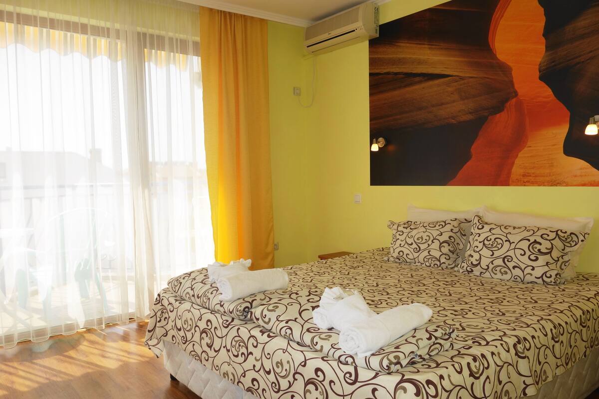 Una habitación de hotel con cama, cortinas, un equipo de aire acondicionado y un mural en la pared.