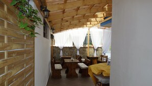 Un espacio comedor exterior cubierto y estrecho, con mobiliario de madera y un muro de piedra de fondo.