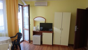 Una habitación con escritorio, televisión, armario, refrigerador pequeño y mesa de comedor con sillas.