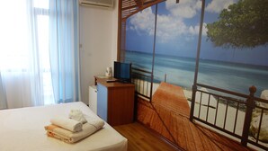 Una habitación de hotel con una cama, un televisor y un mural con motivos playeros en la pared.