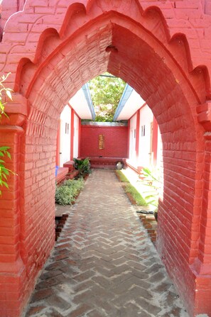 A brick pathway leading through an arched structure with a red brick wall and a white door at the end. - La Casa Di Bagan Nan Eain Thu (Nyaung-U)