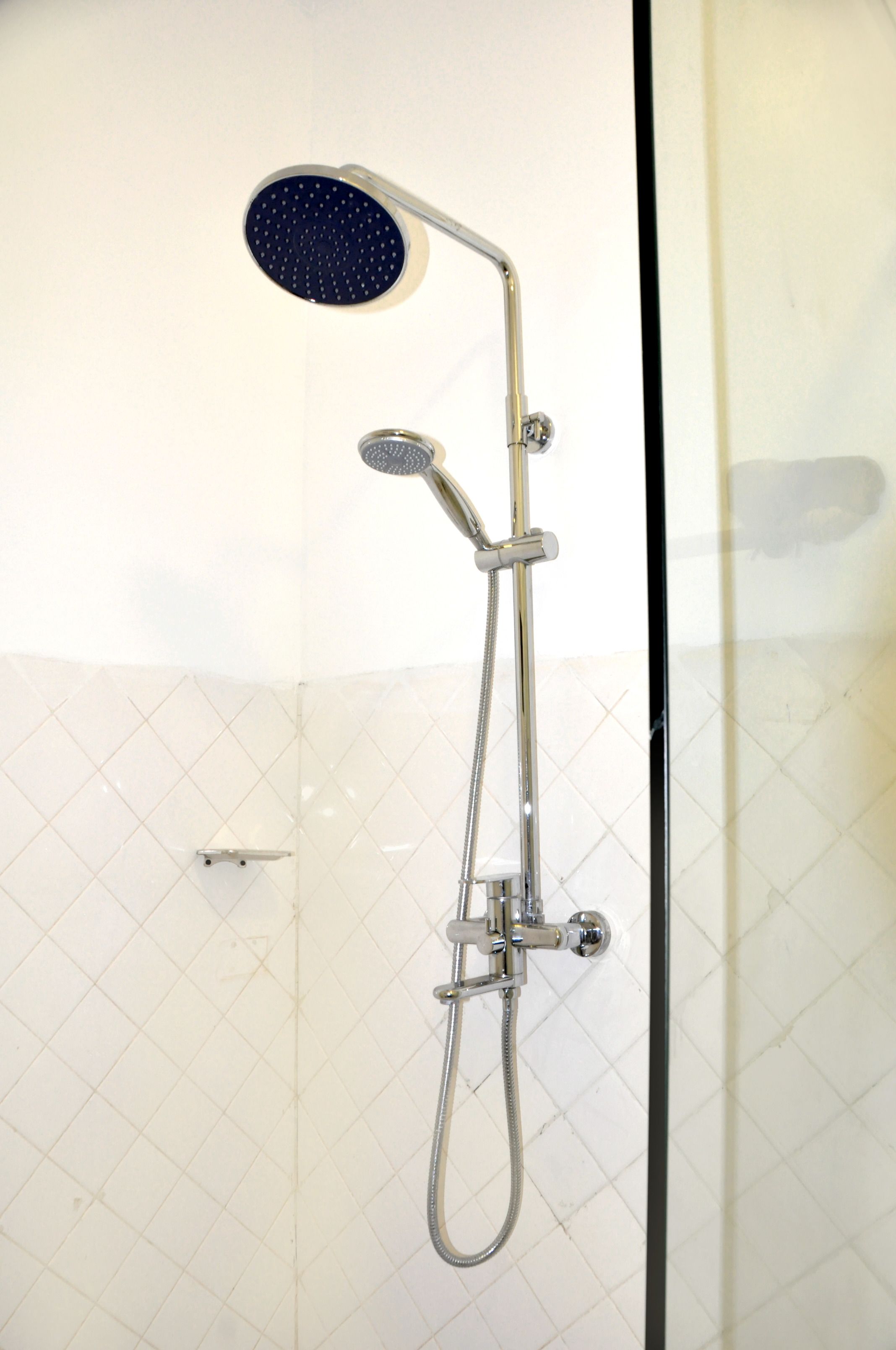 Une douche équipée d’un pommeau de douche à main et d’un pommeau de douche fixe, le tout installé sur un mur avec un sol carrelé.