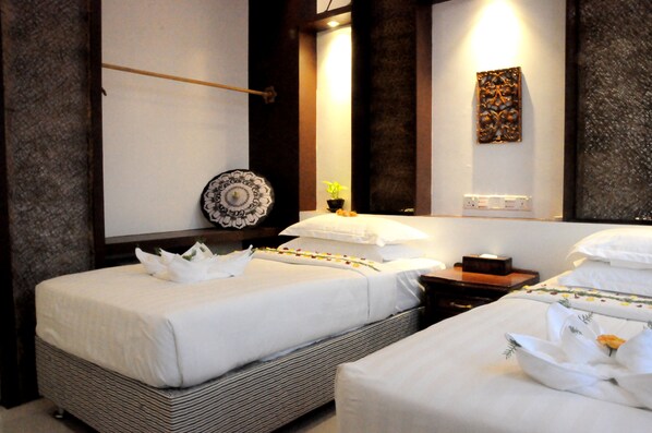 Quarto de hotel com duas camas, uma mesa de cabeceira com abajur, um prato decorativo na parede e uma pequena planta.