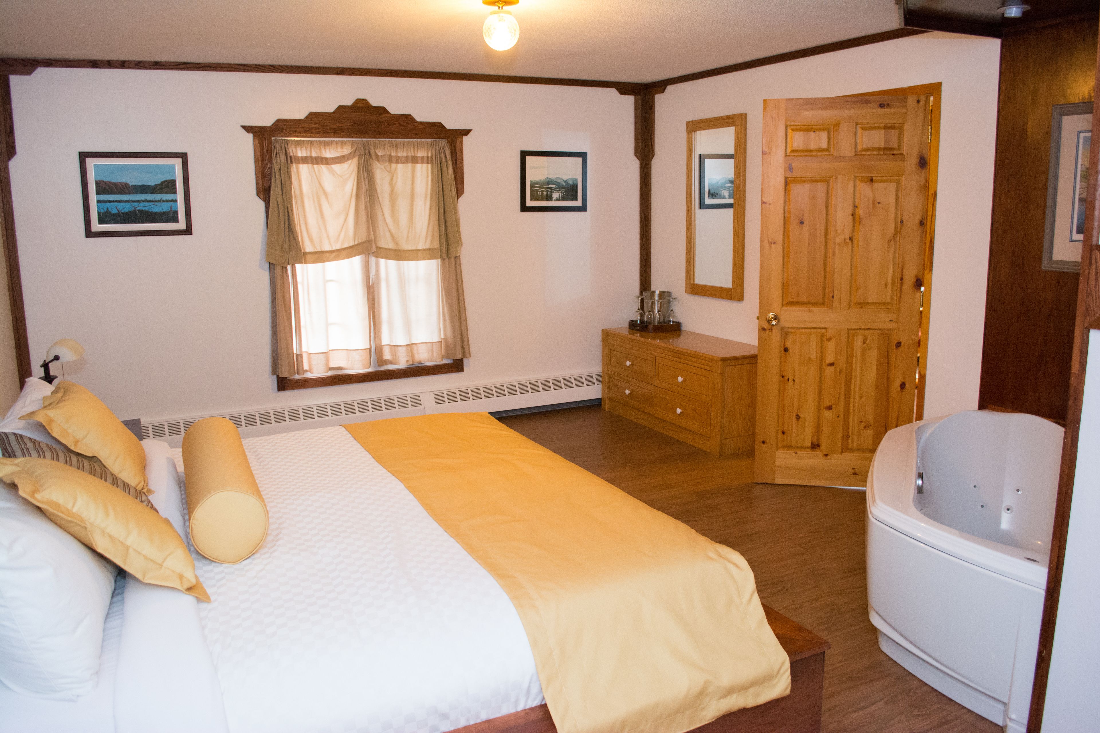Un dormitorio con cama, cómoda de madera, baño con bañera y dos cuadros en la pared.