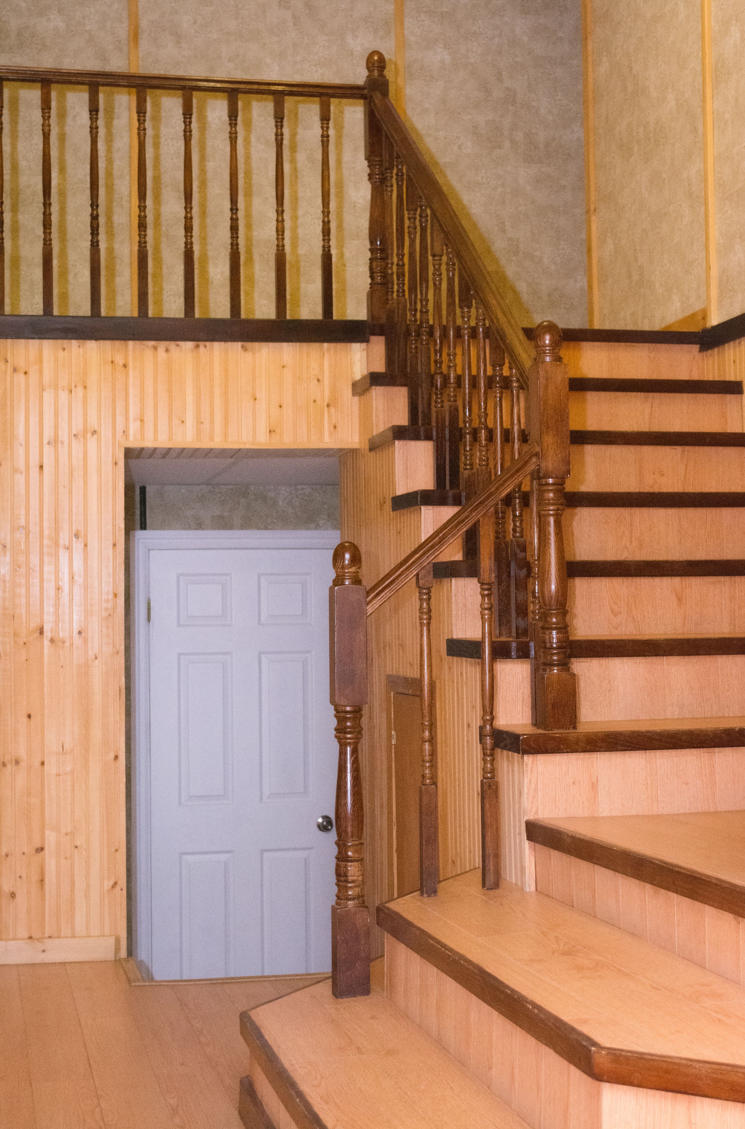 Una escalera de madera con barandilla y una puerta al final.