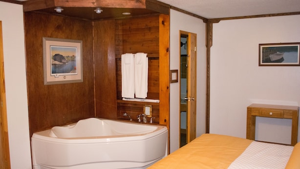 Un baño con bañera, paredes de madera, una cama con colcha amarilla y dos cuadros enmarcados.
