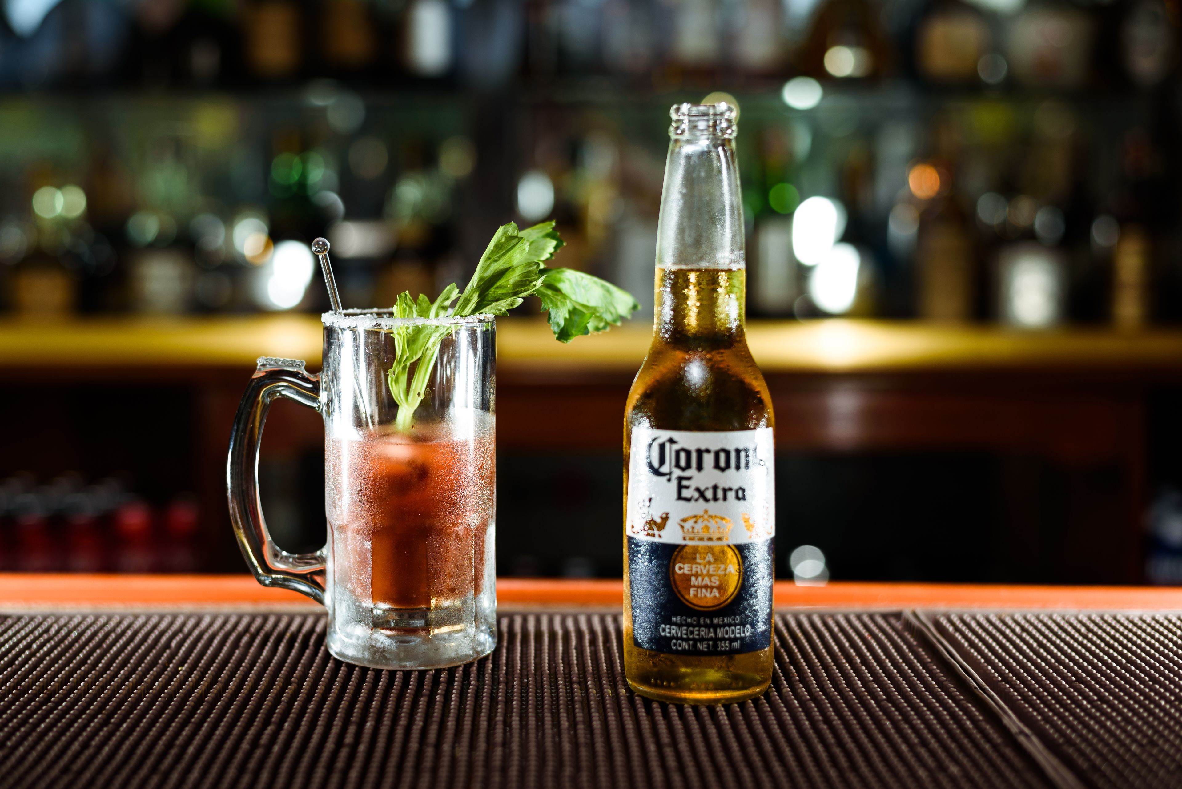 A glass mug with a drink and a bottle of Corona Extra beer on a bar mat.