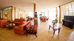 A spacious lobby with orange sofas, a piano, and a bust sculpture. - Hotel & Spa Villa Vergel (Ixtapan de la Sal)